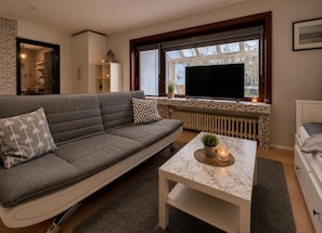 A modern living room with a sofa, a TV, a coffee table, and a window with a view.