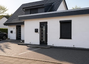 A modern two-story building with a white exterior, black doors, and a tiled roof.
