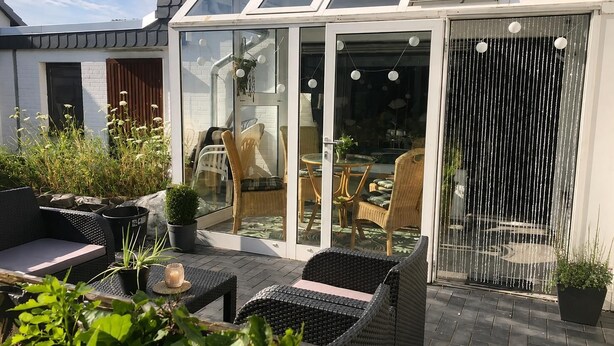 A modern patio with wicker furniture, a glass door leading to an indoor dining area, and a decorative water feature.