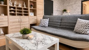 A living room with a grey sofa, a marble coffee table, wooden shelving, and a black door.