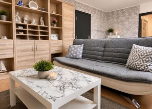 A living room with a grey sofa, a marble coffee table, wooden shelving, and a black door.