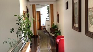 A hallway with a wooden floor, a red bench, and potted plants. - Hotel Ulveira (Oliveira de Frades)
