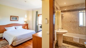 A hotel room with a bed, bedside table, and a bathroom with a sink and bathtub. - Hotel Ulveira (Oliveira de Frades)
