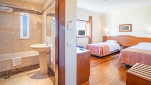 A hotel room with a bathroom, two beds, a wooden headboard, a window, and a painting on the wall. - Hotel Ulveira (Oliveira de Frades)