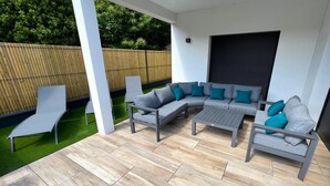Een overdekt terras met een grijze modulaire bank, een losse fauteuil en een kleine tafel.