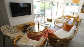Een moderne woonkamer met rieten meubels, een flatscreen televisie en een glazen tafel.