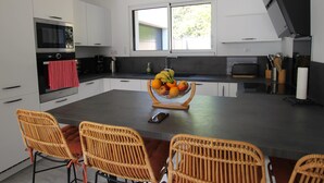 Een moderne keuken met witte kasten, een centraal eiland met een fruitschaal, en rieten stoelen.