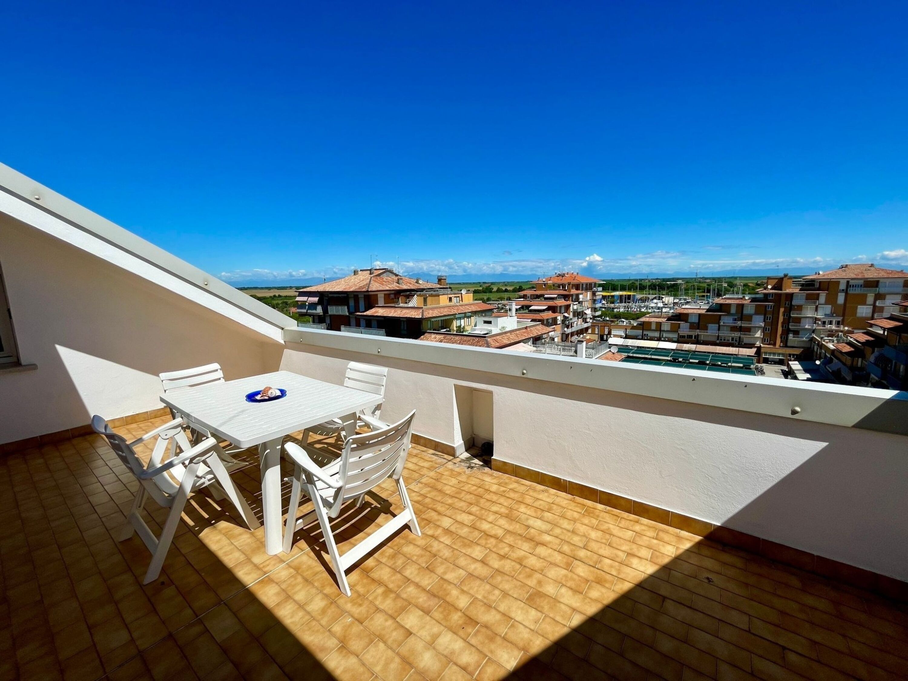 Un balcon avec une table et des chaises, une vue sur les immeubles et un ciel dégagé.