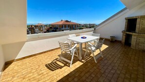A rooftop terrace with a table and chairs, a brick fireplace, and a view of buildings in the distance. - Amazing Flat With sea View Terrace (Caorle)