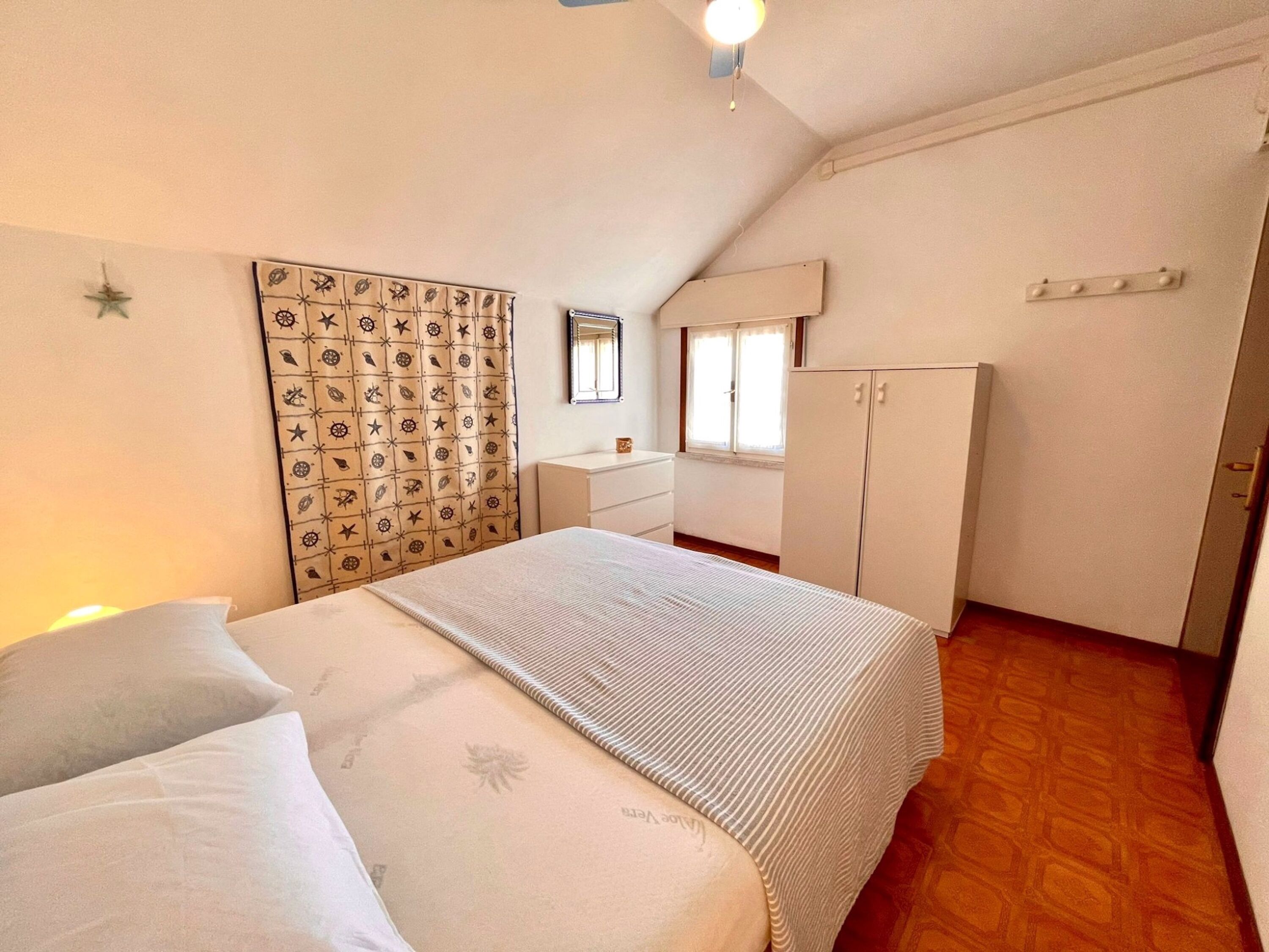 Una camera da letto con un letto, una cassettiera, un armadio, una finestra e una parete con motivo decorativo.
