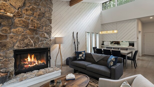 A modern living room with a stone fireplace, a gray sofa, and a dining area with a kitchen in the background.