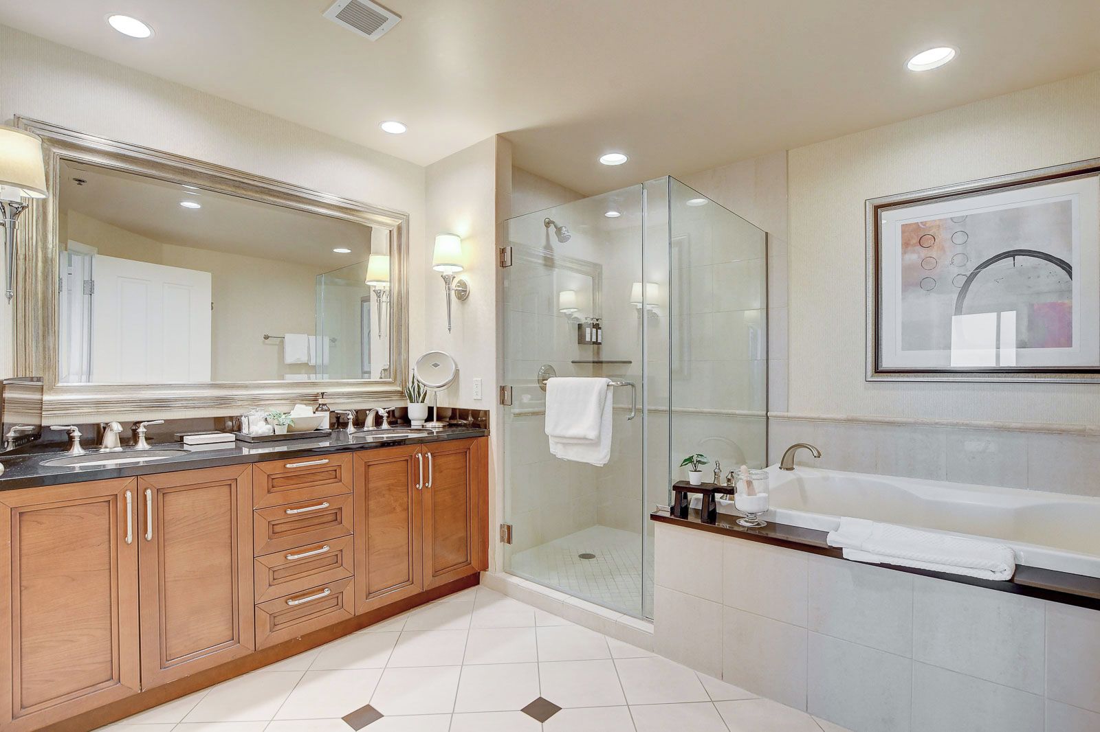 A modern bathroom with a large mirror, wooden cabinets, a glass shower enclosure, and a white sink.