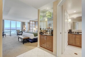 A hotel room with a large bed, a sitting area with a view, a bathroom with wooden cabinets, and a large window. - Classic Suite Signature Resort Pool View (Las Vegas)