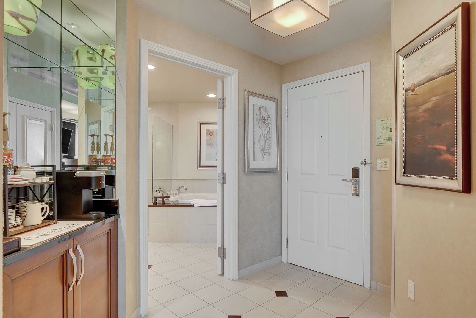 A hallway leading to a bathroom with a sink, a framed picture on the wall, and a door with a handle.