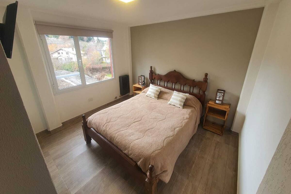 Quarto com cama de madeira, uma janela grande e uma luminária no teto.