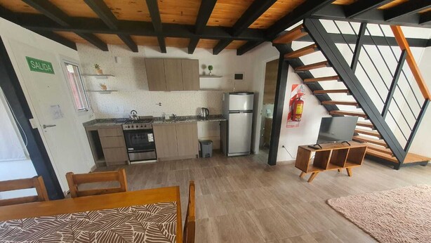 Cozinha compacta com eletrodomésticos modernos, área de refeições com mesa estampada e escada para um andar superior.