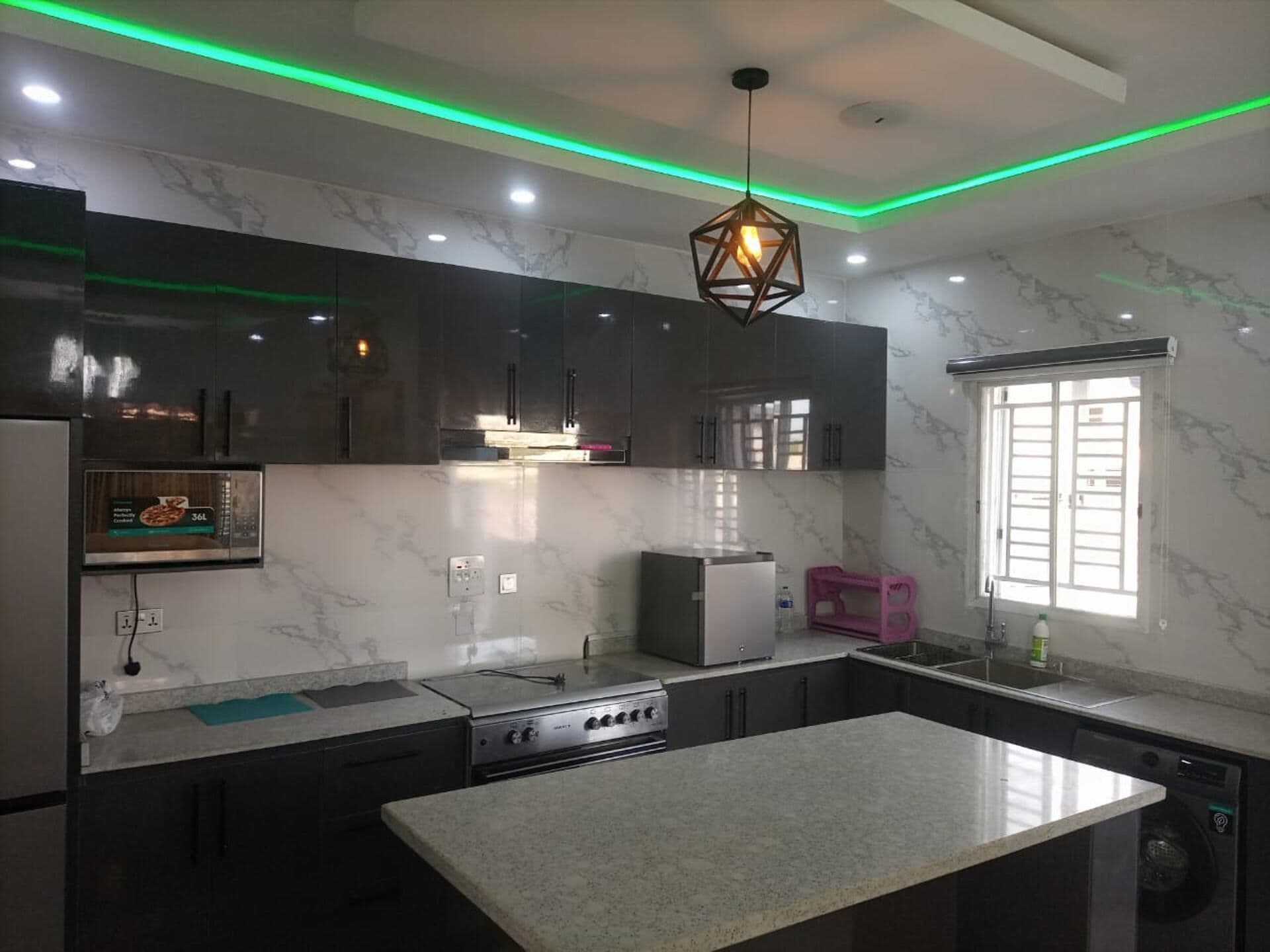 Una cocina moderna con armarios oscuros, una isla central, horno empotrado y una ventana con persianas.