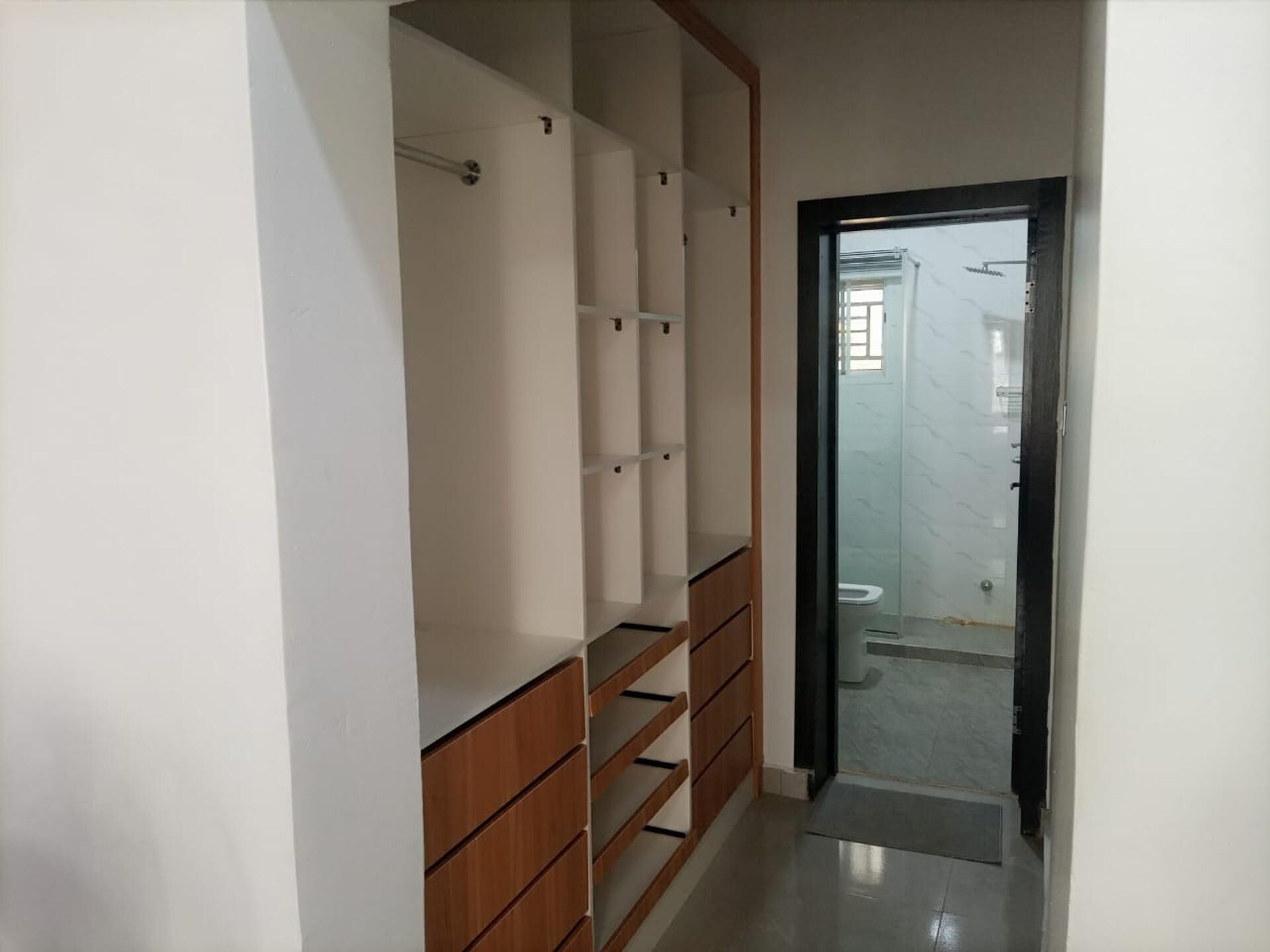 Een gang met een houten garderobe en een badkamer zichtbaar door een glazen deur.