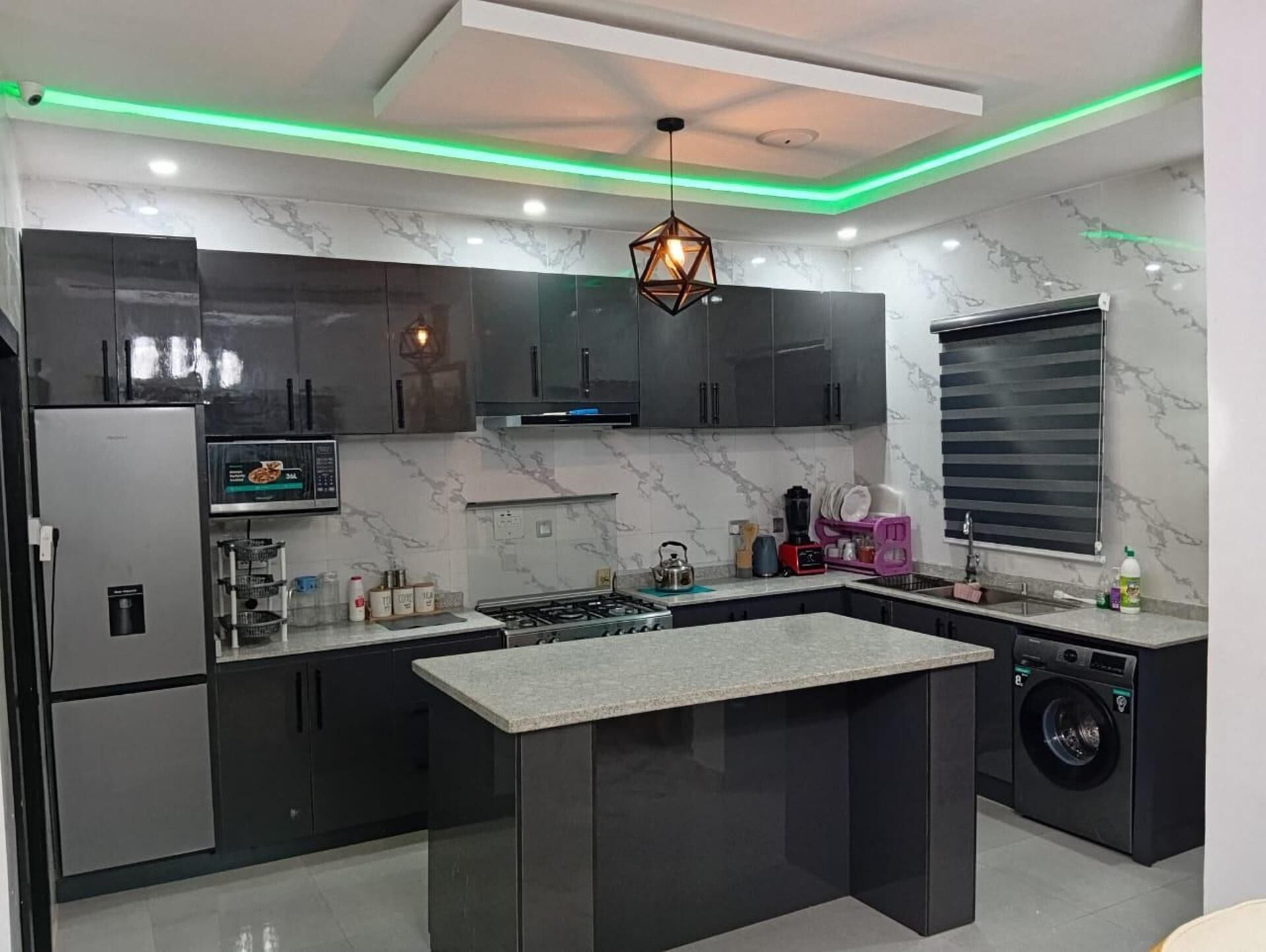 A modern kitchen with a central island, stainless steel appliances, and a unique geometric pendant light.