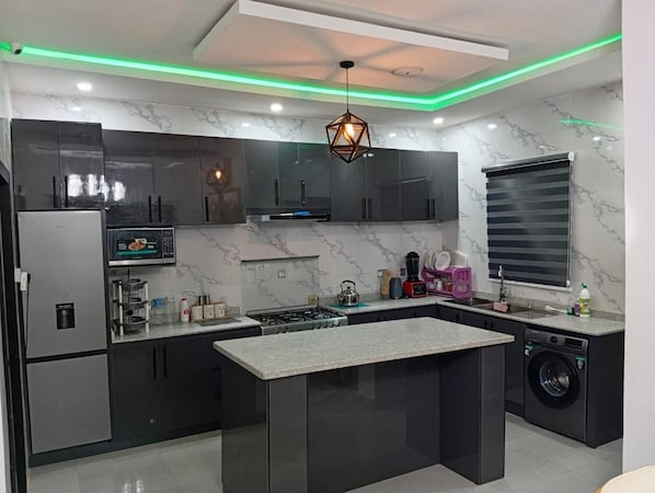 A modern kitchen with a central island, stainless steel appliances, and a unique geometric pendant light.