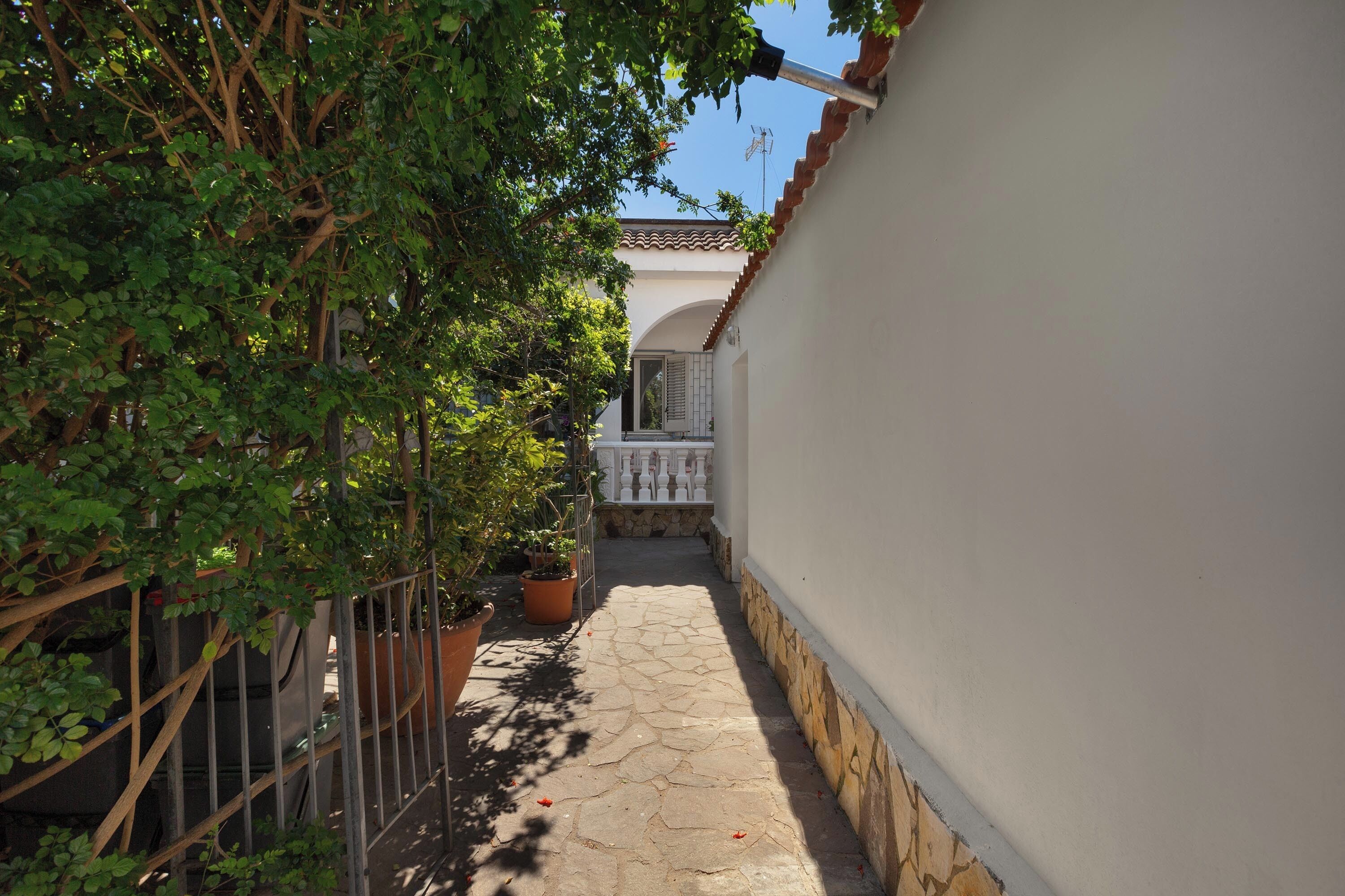 Un stretto sentiero in pietra che conduce a un edificio con pareti bianche, tetto in tegole e un balcone.