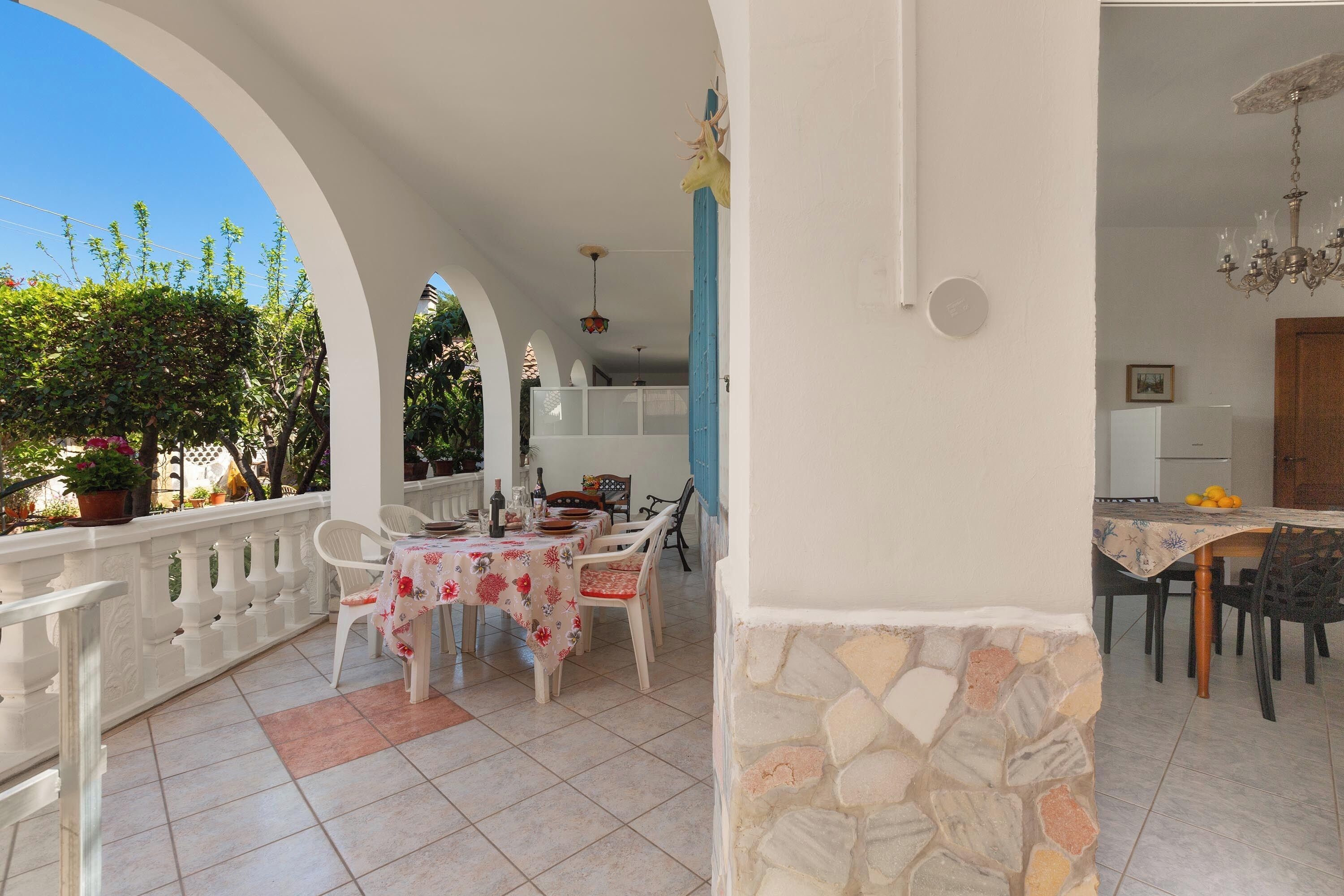 A covered patio with a dining table set for four, surrounded by white chairs.