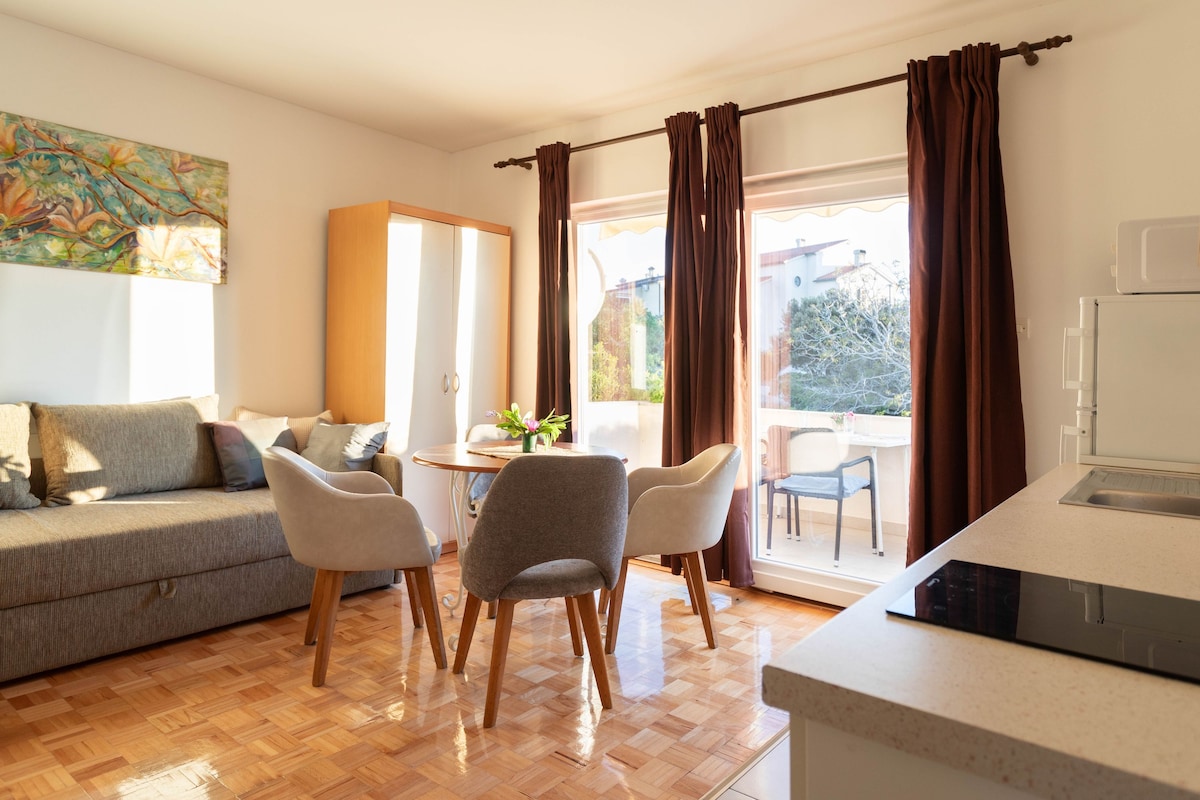 A modern living room with a sofa, two chairs, a dining table, and a kitchen area.