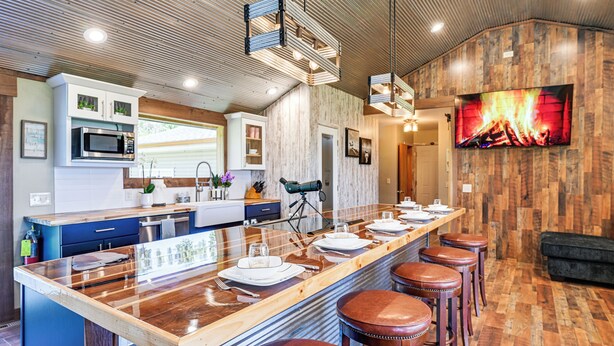 A modern kitchen with a large island, bar stools, and a flat-screen TV mounted on the wall.