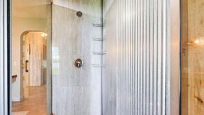 A modern shower with a glass door, a metal showerhead, and a built-in shelf.