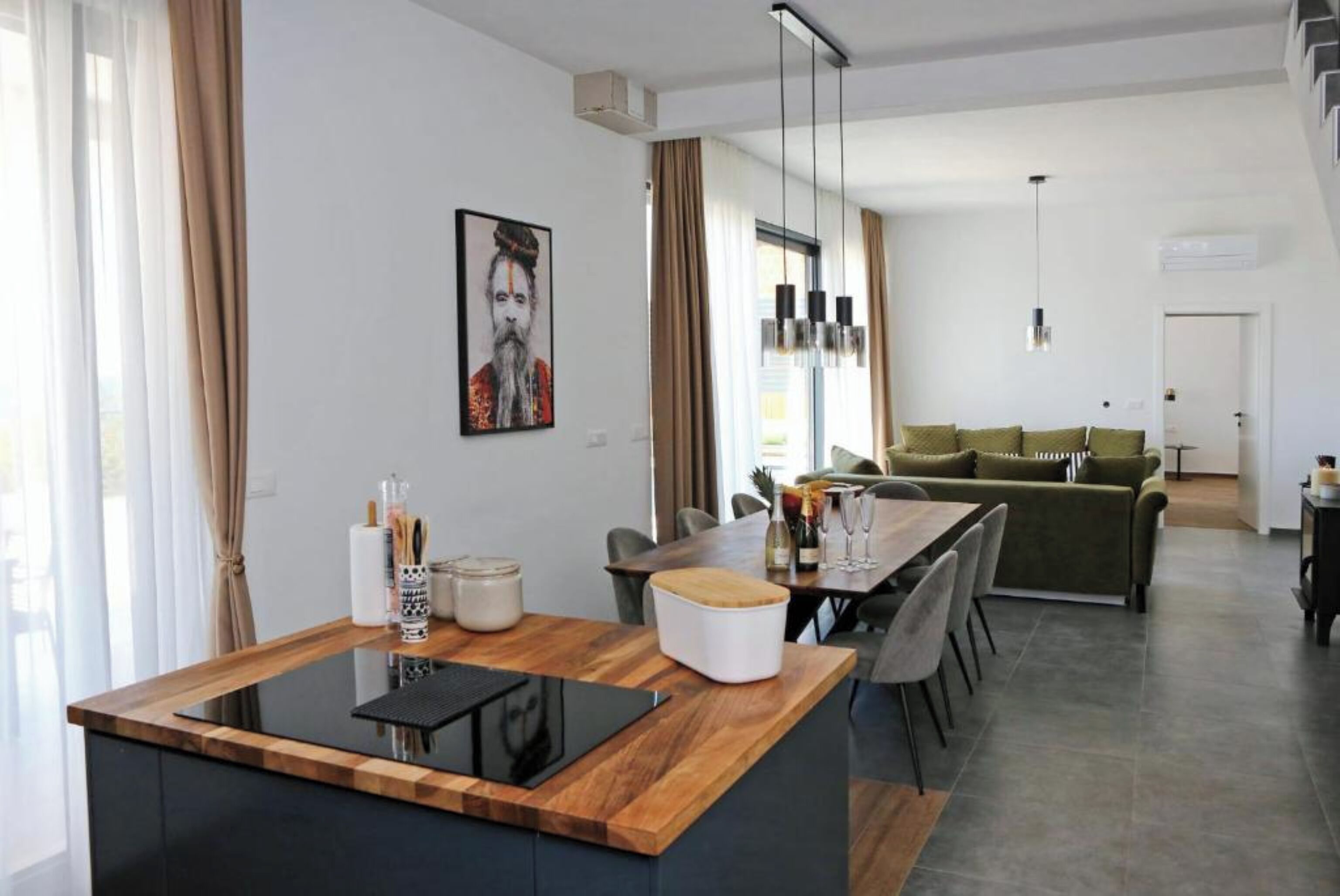 A modern kitchen with a wooden countertop, a dining area with a table and chairs, and a green sofa in the background.
