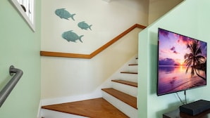 A staircase with wooden steps and a handrail, a wall with three fish decorations, and a TV displaying a sunset scene. - Enjoy the quiet and walk to downtown! (Cedar Key)