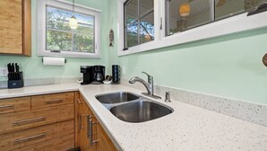 A kitchen with two stainless steel sinks, wooden cabinets, and a window with blinds. - Enjoy the quiet and walk to downtown! (Cedar Key)