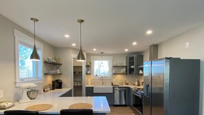 Cozinha moderna com ilha central, duas luminárias pendentes, geladeira e piso de madeira.