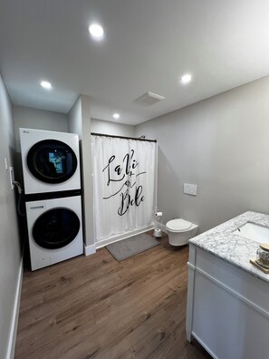 A modern bathroom with a shower curtain featuring a motivational phrase, a toilet, and a washing machine. - Spacious 2 Bedroom Apartment on Rural, Wooded Property.  King Bed (Bow)