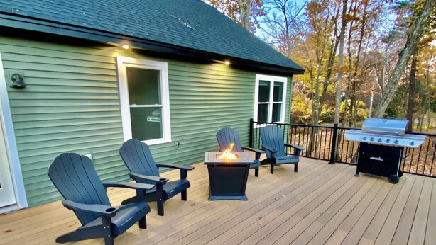 Um deck com cadeiras Adirondack, um braseiro e uma churrasqueira.