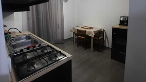 Cocina compacta con estufa a gas, un lavamanos y una zona de comedor con mesa y sillas.