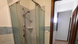 Un área de ducha con paredes de vidrio, un banco, paredes alicatadas y una puerta de madera que da a otra habitación.