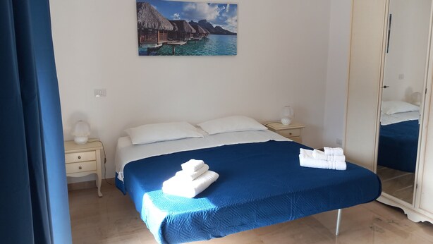 Un dormitorio con una cama, una mesita de noche, un espejo y un cuadro con una playa.