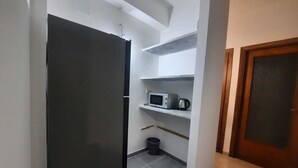 Cocina compacta con refrigerador, microondas y cafetera sobre estantes.