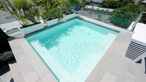 A rectangular pool with clear blue water, surrounded by light-colored tiles and potted plants.