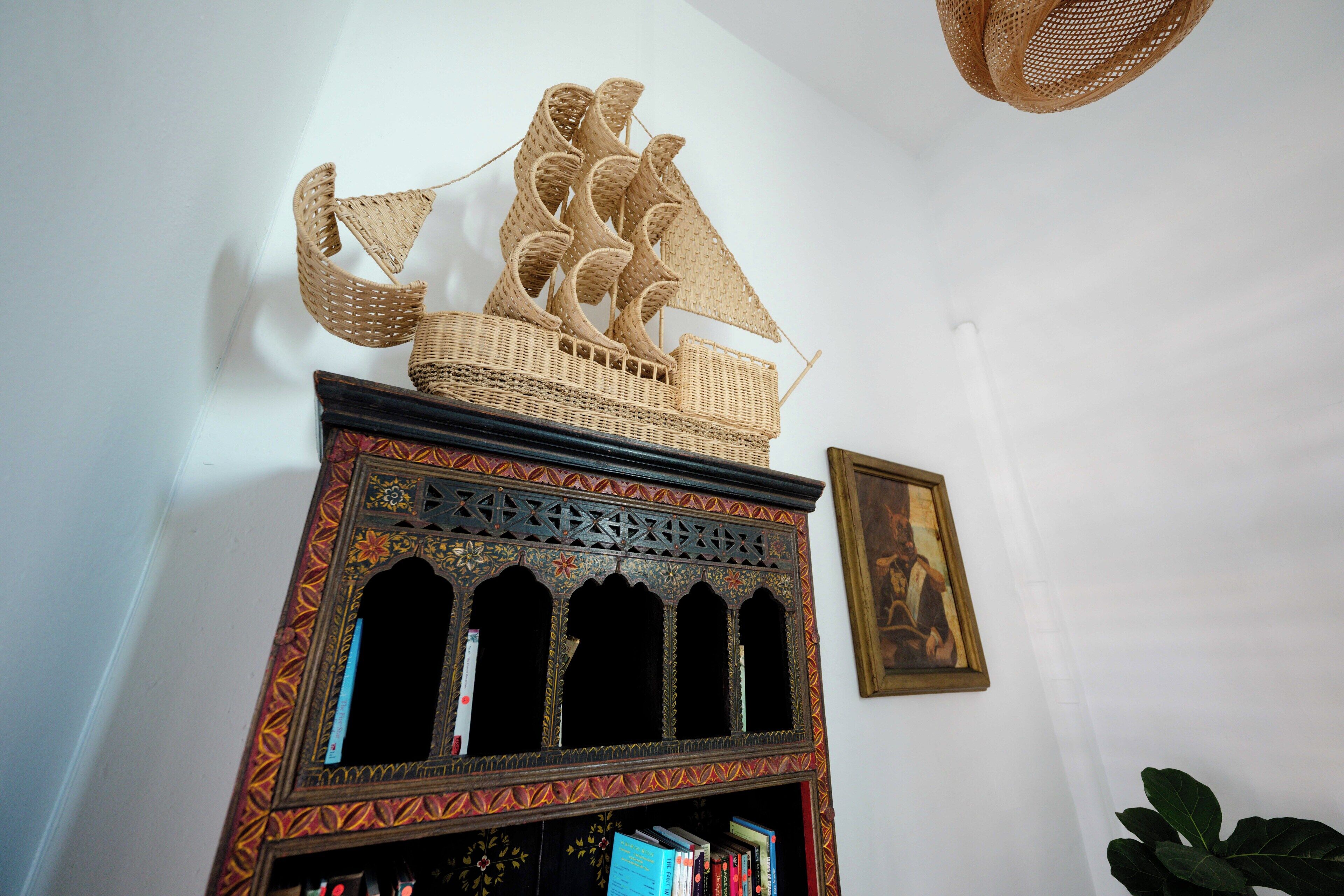 A decorative ship model on a shelf, a framed painting on the wall, and a potted plant in the corner.