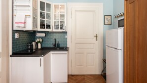 Une cuisine de taille réduite avec des meubles blancs, un plan de travail noir et un réfrigérateur blanc.