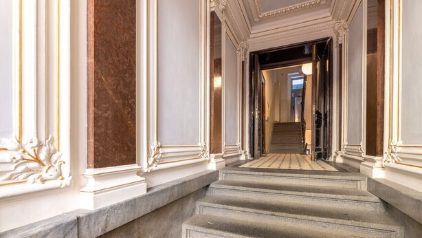 Un magnifique escalier en marbre, orné de colonnes blanches décoratives, mène à un couloir bien éclairé.