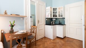 Une cuisine compacte avec des meubles blancs, une table à manger en bois et un parquet à motifs en chevrons.