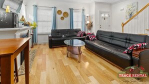 Un salon moderne avec un canapé en cuir noir, une table basse en verre et une table d’appoint en bois.