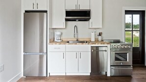 A modern kitchen with white cabinets, stainless steel appliances, a built-in microwave, and a window providing a view of the outdoors. - 2 Bedroom Beacon Cottage 3 - Two bedrooms, one sleeper sofa and a kitchenette (Allons)