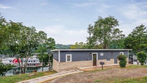 A small cabin-style building with a stone foundation and a wooden exterior, located near a body of water with boats visible in the background. - 2 Bedroom Beacon Cottage 3 - Two bedrooms, one sleeper sofa and a kitchenette (Allons)
