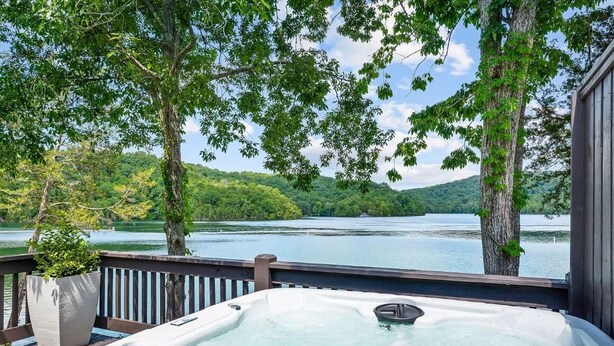 Ein Whirlpool auf einer Terrasse mit Blick auf einen See, Bäume und Hügel im Hintergrund.