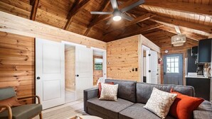 Ein gemütliches Wohnzimmer mit grauem Sofa, Holzwänden und einem Deckenventilator.