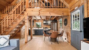 A wooden cabin interior with a staircase leading to a loft, a kitchen with modern appliances, and a dining area with chairs and a table. - Eagle's Perch Cabin 13 with Loft - One bed in loft, sleeper sofa and full kitchen (Allons)